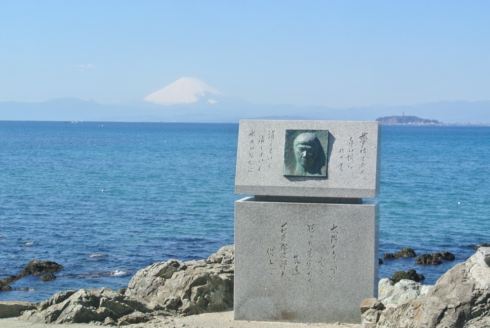 岩場にたてられた裕次郎碑。裕次郎の顔が刻まれている。後ろには青い海と富士山がみえる。
