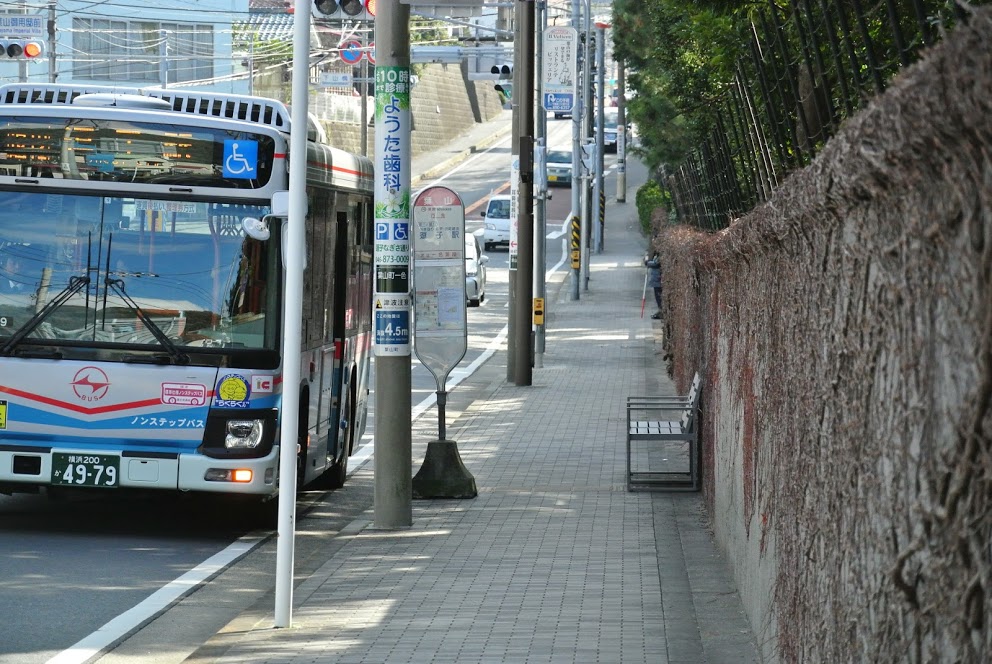 御用邸石塀。バス停「葉山」には青いバスが停車している