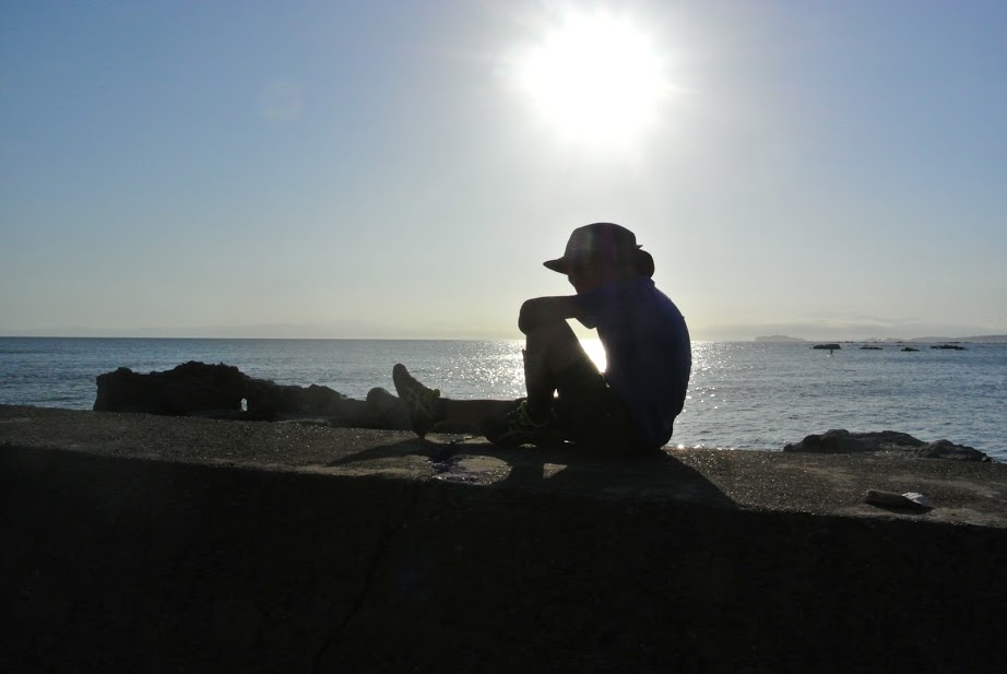 防波堤の上に少年が一人座っている。逆光で輪郭だけが黒く映り、幻想的な1枚。